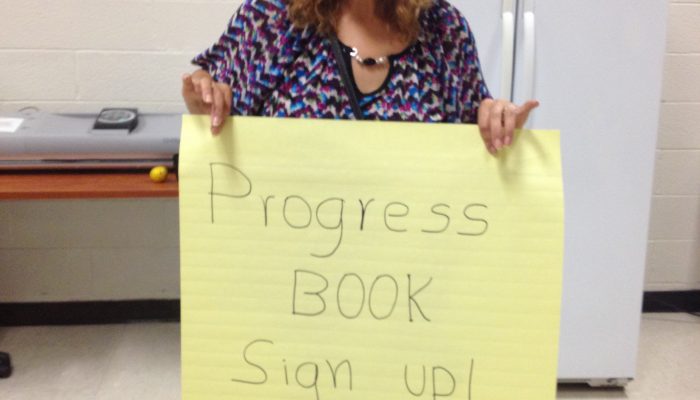 Woman holding a poster reading "Progress Book Sign up! Free Coffee"